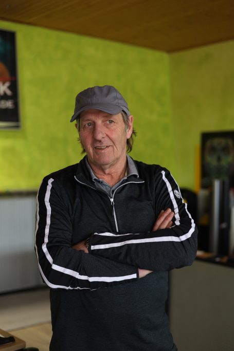 Mann mit Mütze, gekreuzten Armen und sportlichem Outfit steht in einem hellen Raum.